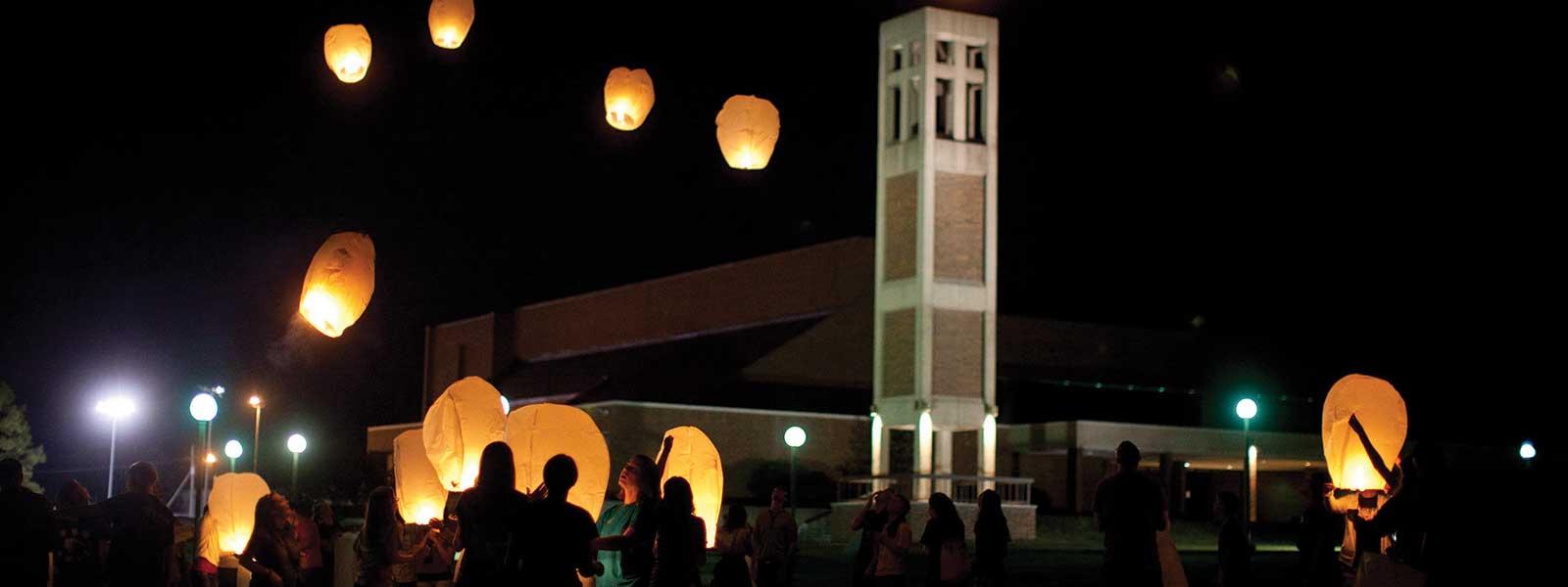 students release lanterns into night sky in front of bell tower